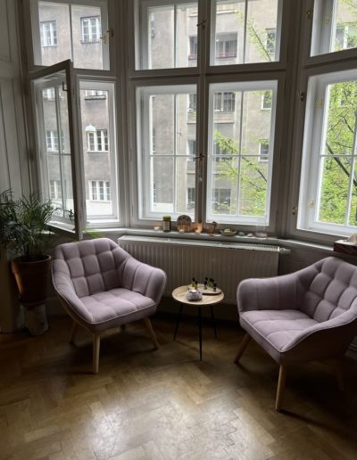 Dvě fialová křesla u stolku s oleji před rohovým oknem